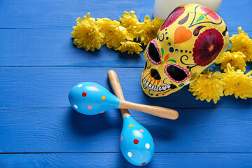 Painted human skull for Mexico's Day of the Dead (El Dia de Muertos), maracas and flowers on color...