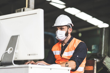 Young caucasian engineering man worker working on digital tablet computer at manufacturing. Worker man wearing face mask prevent covid-19 virus and protective hard hat.