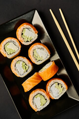 Sushi rolls lie on a black plate with wooden sticks on a black background.