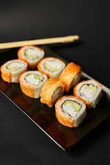 Sushi rolls lie on a black plate with wooden sticks on a black background.