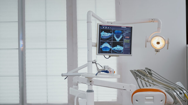 Close up of medical orthodontist display with teeth x ray images on it. Empty professional hospital office stomatology chair with nobody in it. Closeup of dental drill instrument ready for tooth care