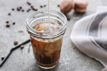 Pouring of milk into glass with hot coffee on grunge background
