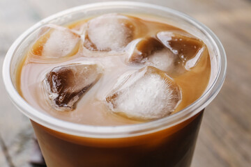 Plastic cup of ice coffee on wooden background, closeup