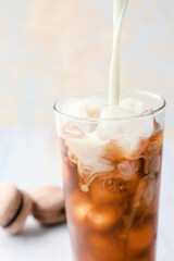 Pouring of milk into glass of hot coffee with ice on light background