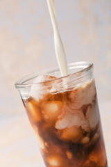 Pouring of milk into glass of hot coffee with ice on light background