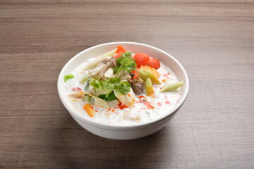 cook hot and spicy white coconut curry laksa soup with mushroom and mixed vegetables in white bowl on wood background asian halal vegan menu