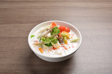 cook hot and spicy white coconut curry laksa soup with mushroom and mixed vegetables in white bowl on wood background asian halal vegan menu