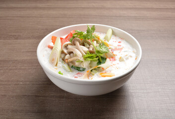 cook hot and spicy white coconut curry laksa soup with mushroom and mixed vegetables in white bowl on wood background asian halal vegan menu