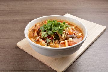 cook hot and spicy tom yum soup with mushroom and mixed vegetables in white bowl on wood background...