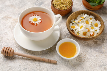 Composition with cup of chamomile tea, flowers and honey on light background