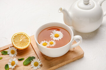 Composition with cup of chamomile tea and teapot on light background