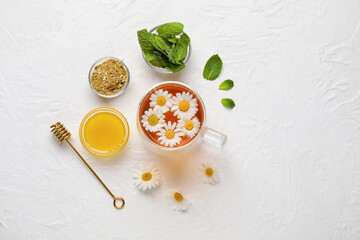 Composition with cup of chamomile tea, flowers, mint and honey on light background