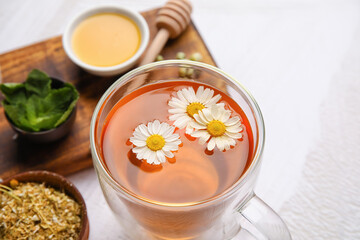 Composition with cup of chamomile tea, honey, mint leaves and dried flowers on light background
