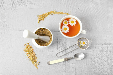 Composition with cup of chamomile tea and dried flowers on light background
