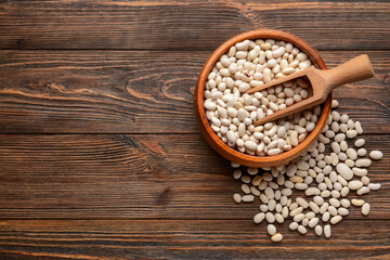 Bowl and scoop with raw beans on wooden background