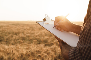 Man making notes on clipboard while standing in wheat field