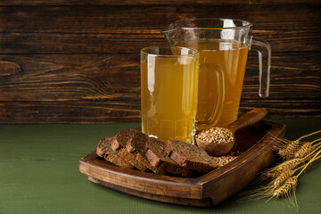 Mug and jug of fresh kvass on color wooden background