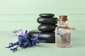 Obraz na płótnie Canvas Bottle of lavender essential oil, spa stones and flowers on color wooden background