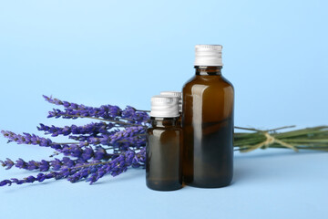 Bottles of lavender essential oil and flowers on color background