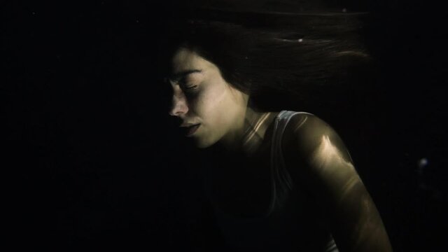 Woman with eyes closed underwater at night