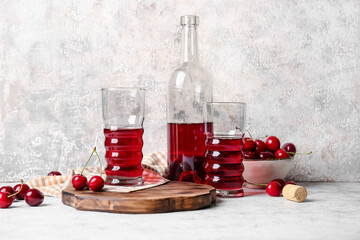 Glasses and bottle of sweet cherry wine on light background