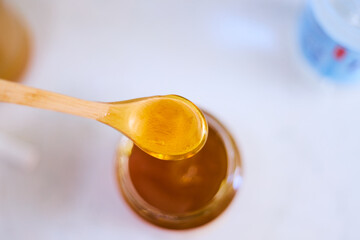 A wooden teaspoon over a jar of honey, honey dripping from the spoon into the glass jar close-up