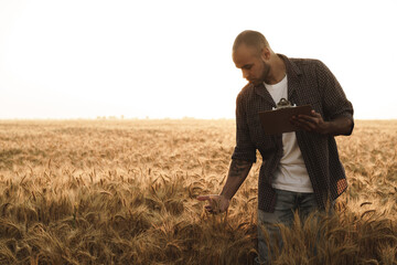 Naklejka na ściany i meble Man making notes on clipboard while standing in wheat field