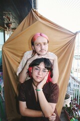 portrait of happy smiling couple / gender queer friends pink hairstyle & fashion with brown background home photoshoot *3