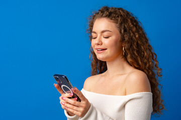 Young curly woman using her smartphone against blue background