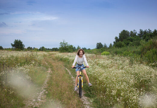 funny portrait of emotional pretty girl 17-18 years old on a bicycle in motion. having fun riding a bike in the picturesque flowering fields. healthy active lifestyle. cycling outdoors. digital detox