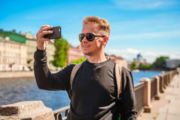 A young man walks along the embankment in St. Petersburg with beautiful views of bridges and canals.