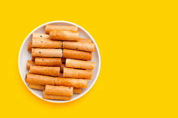 Thai crispy coconut rolls in white plate on yellow background.