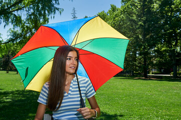 young woman protects herself from the sun with a multi-colored umbrella in the park
