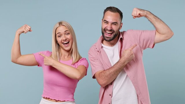 Strong sporty fitness fun young couple two friends family in pink clothes together strong woman bearded man showing biceps muscles isolated on pastel plain light blue color background studio portrait