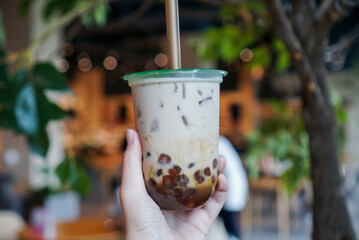 Iced milk tea with coconut sugar. Hand holding a plastic cup of milk tea mixed with coconut sugar syrup, served with tapicoca pearls.