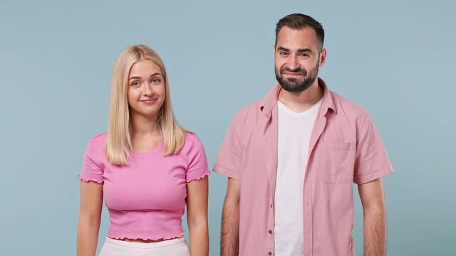 Confused shy shamed young couple two friends family bearded man woman in pink clothes together spreading hands say oops i am sorry isolated on pastel plain light blue color background studio portrait