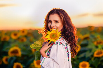 Beautiful woman enjoying nature in the sunflower field at sunset. Traditional clothes. Attractive brunette woman with long and healthy hair. - obrazy, fototapety, plakaty