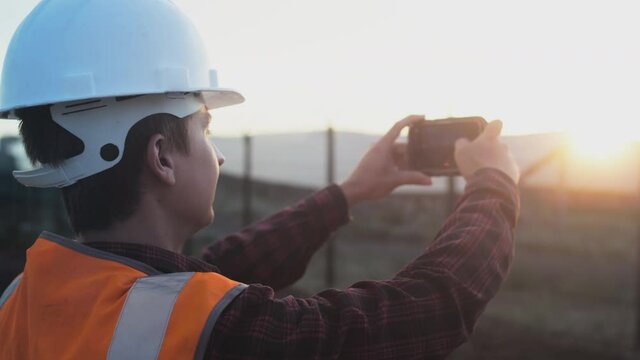 A male engineer takes a photo of a plantation or solar panel plant on a smartphone. Inspects and checks the quality of the installation. Renewable energy technologies. Combating global warming.