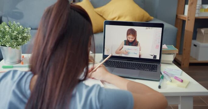 Young Asia girl with casual use computer laptop video call learn online with teacher write lecture notebook living room at house. Isolate education online e-learning coronavirus pandemic concept.