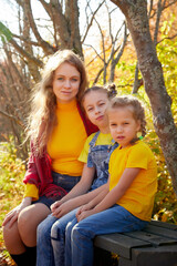 Two young little girl and his mother with blonde hair in an autumn park on a yellow and orange leaf background. Family walking in forest