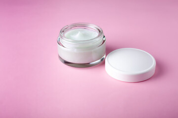 Glass jar and white cap with body cream on pink background. Cosmetic product for skin care. Transparent jar with face cream isolated.