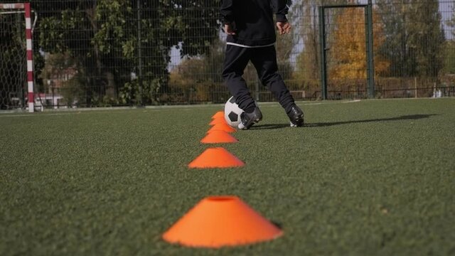 A little boy trains in dribbling between orange cones on the soccer field.