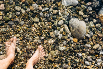 Sea waves on a stone beach covering the rocks and male feet. Summer rest and vacancy concept.