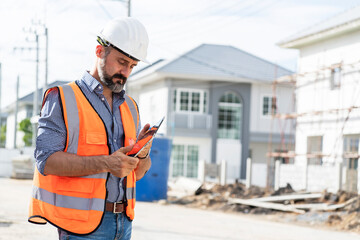 Foreman wearing an engineer helmet holding a tablet inspects construction work at a construction...