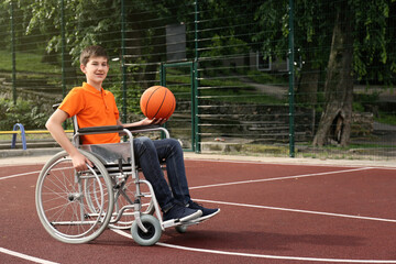 Disabled teenage boy in wheelchair with basketball ball at outdoor court