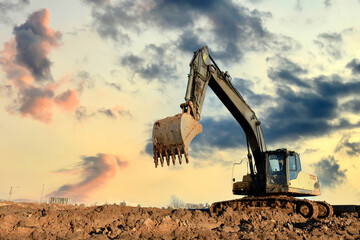 Excavator on earthworks at construction site on sunset background. Heavy machinery and equipment for earthmoving - obrazy, fototapety, plakaty