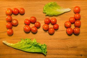 Tomatoes and lettuce on a wooden table. Tomatoes form the word 