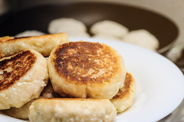 Cheese pancakes in a plate on the background of a frying pan in a close-up in the dark