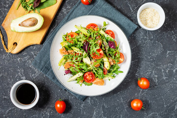 Salmon salad with green leaves, avocado and cherry tomato on black stone background. Top view