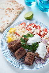Blue and white plate with grilled kofta kebabs, couscous, yogurt, red tomatoes and lavash, vertical shot, selective focus